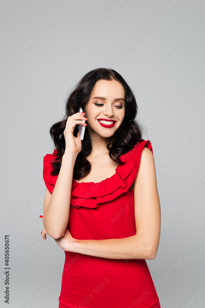 Fototapeta premium cheerful woman with red lips talking on smartphone isolated on grey
