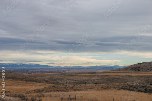 Asphalt road among steppes with yellow dry grass, blue mountains on the horizon, beautiful blue-gray autumn sky. Montana, USA, 11-23-2019