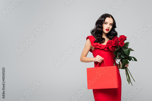 young woman holding shopping bag and red roses isolated on grey