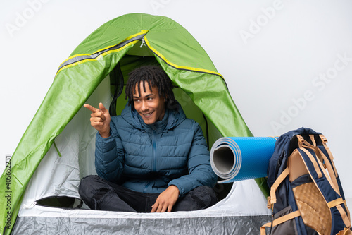 Young african american man inside a camping green tent pointing finger to the side and presenting a product