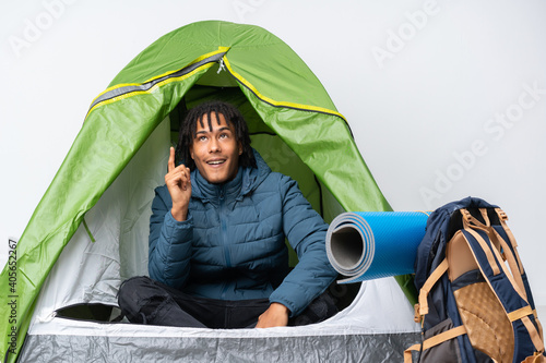 Young african american man inside a camping green tent pointing up and surprised