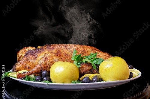 Roast duck with apples, lemon, olives and herbs on a black background