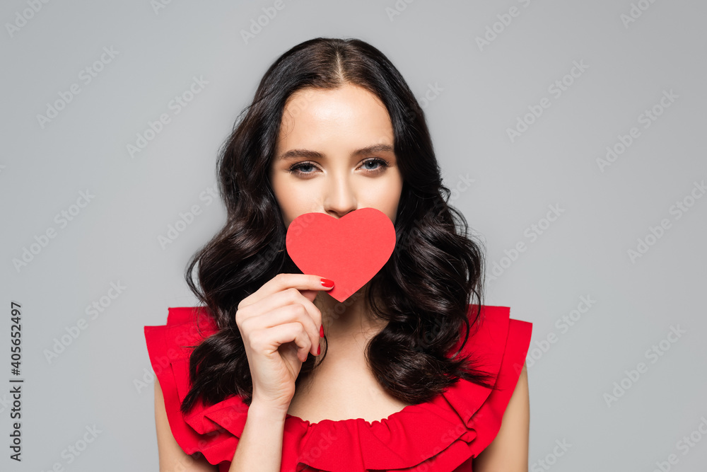 young woman covering mouth with red paper heart isolated on grey