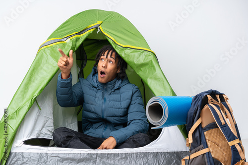 Young african american man inside a camping green tent pointing away