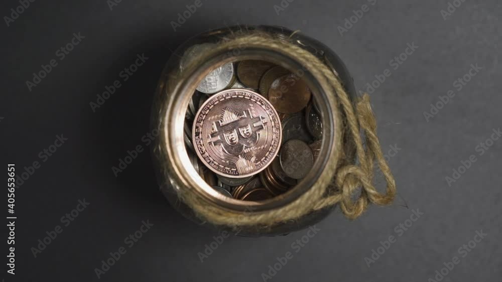 Close-Up of Bronze Bitcoin drop in Piggy Bank Jar of Coins with White Background Close-Up of Bronze Bitcoin drop in Piggy Bank Jar of Coins with White Background
