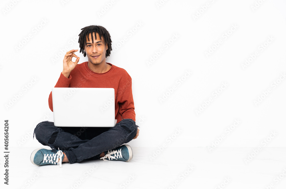 Young african american man sitting on the floor and working with his laptop showing ok sign with fingers Young african american man sitting on the floor and working with his laptop showing ok sign with fingers
