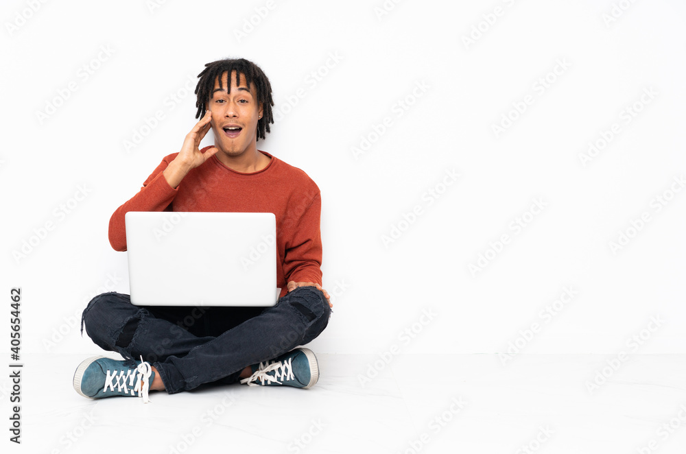 Young african american man sitting on the floor and working with his laptop with surprise and shocked facial expression Young african american man sitting on the floor and working with his laptop with surprise and shocked facial expression