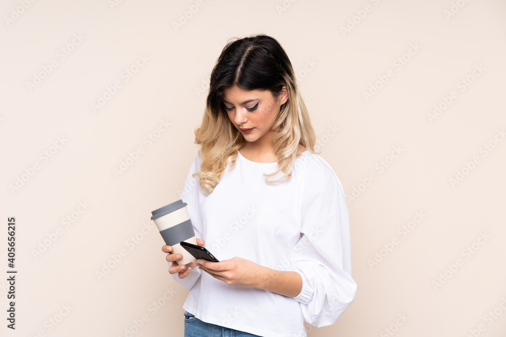 Teenager girl isolated on beige background holding coffee to take away and a mobile Teenager girl isolated on beige background holding coffee to take away and a mobile