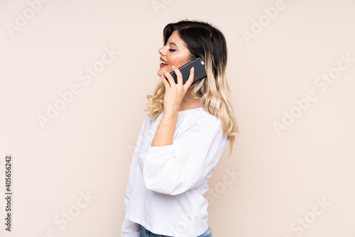 Teenager girl isolated on beige background keeping a conversation with the mobile phone