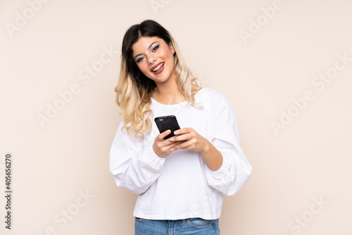 Teenager girl isolated on beige background sending a message with the mobile