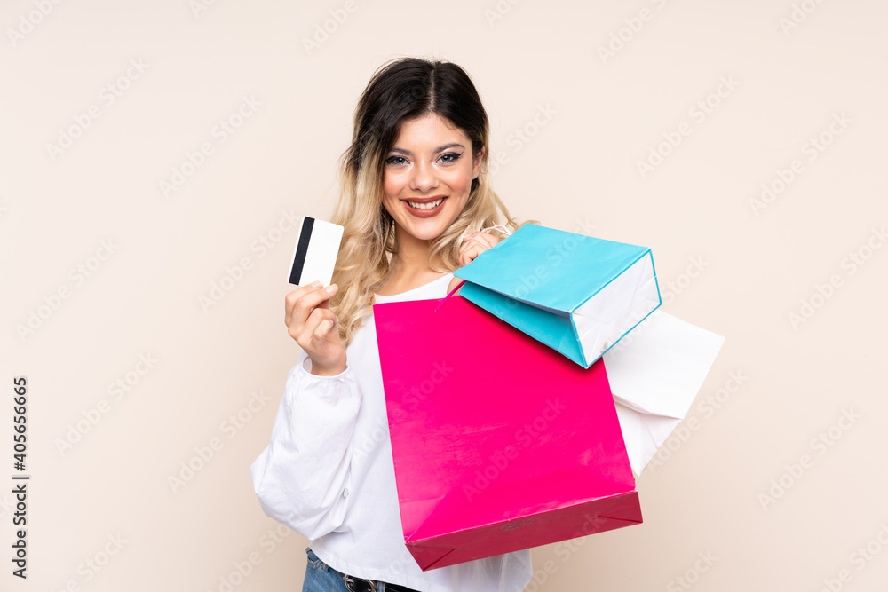 Teenager girl isolated on beige background holding shopping bags and a credit card Teenager girl isolated on beige background holding shopping bags and a credit card