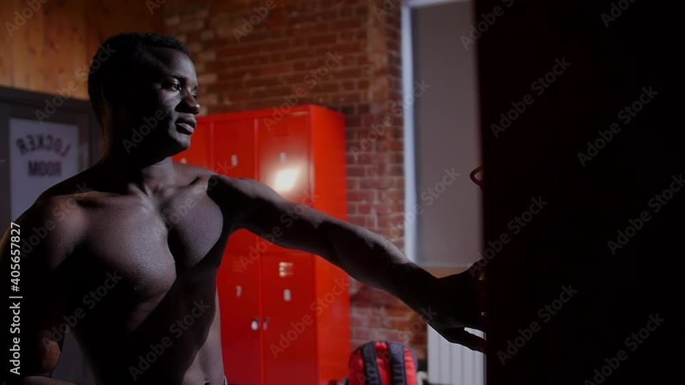 African-american athletic naked young man opens up his locker in locker room