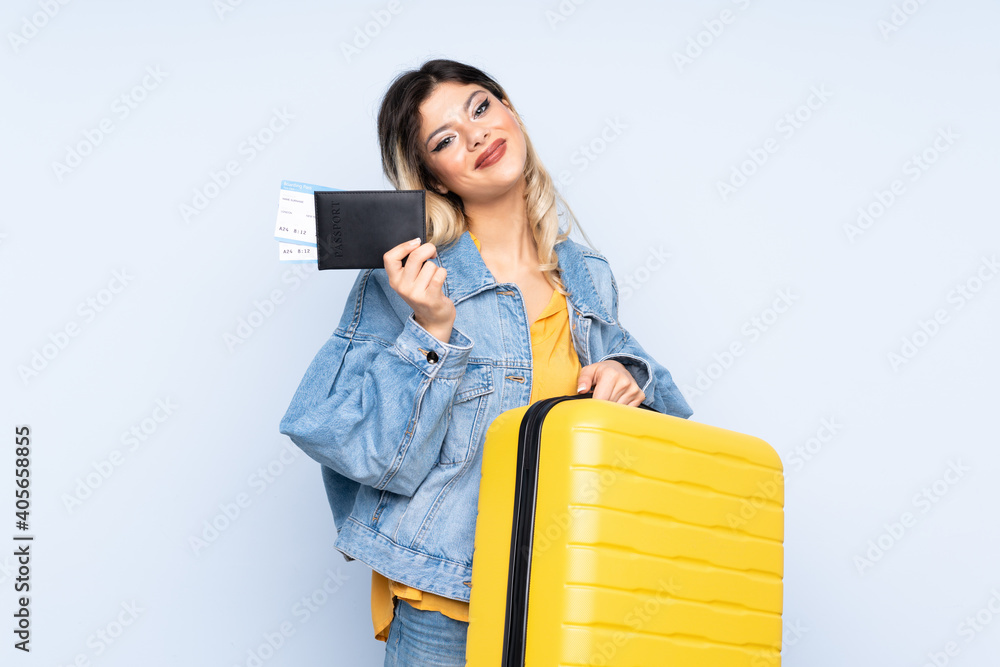Traveler teenager holding a suitcase isolated on blue background in vacation with suitcase and passport