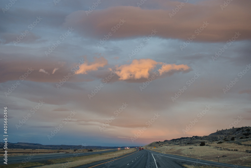 Autumn landscape at dusk. Asphalt road among steppes with yellow dry grass, blue mountains on the horizon, beautiful blue-gray autumn sky. Montana, USA, 11-23-2019
