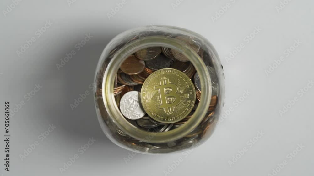Close-Up of Gold Bitcoin drop in Piggy Bank Jar of Coins with White Background Close-Up of Gold Bitcoin drop in Piggy Bank Jar of Coins with White Background