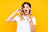 Teenager girl isolated on yellow background holding colorful French macarons and surprised while pointing front