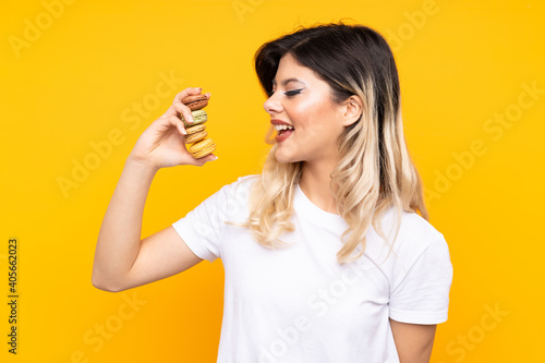Teenager girl isolated on yellow background holding colorful French macarons and celebrating a victory