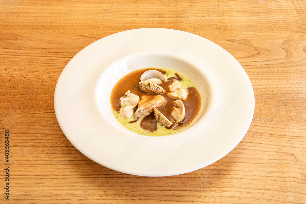 delicious fish soup with clams in white plate on wooden table delicious fish soup with clams in white plate on wooden table