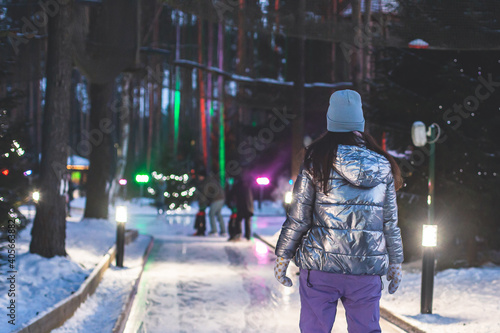 Girl ice skating on the ice rink arena with happy people in the background, concept of ice skating in winter, winter activities, holiday christmas time, with new year decoration and illumination