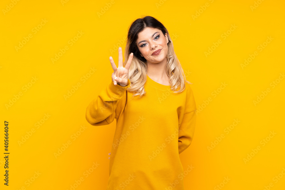 Teenager girl isolated on yellow background happy and counting three with fingers Teenager girl isolated on yellow background happy and counting three with fingers