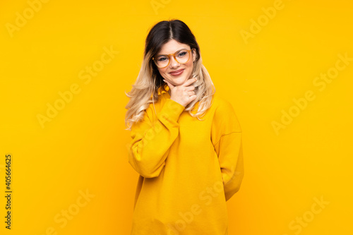 Teenager girl isolated on yellow background with glasses and smiling © luismolinero