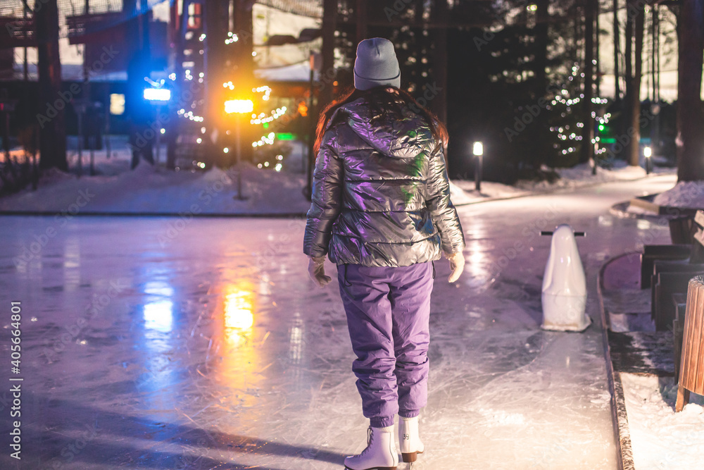 Obraz premium Girl ice skating on the ice rink arena with happy people in the background, concept of ice skating in winter, winter activities, holiday christmas time, with new year decoration and illumination