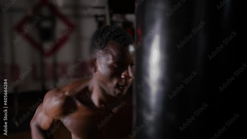 African-american athletic half-naked young man boxer training punching on the punching bag with an effort in the gym African-american athletic half-naked young man boxer training punching on the punching bag with an effort in the gym