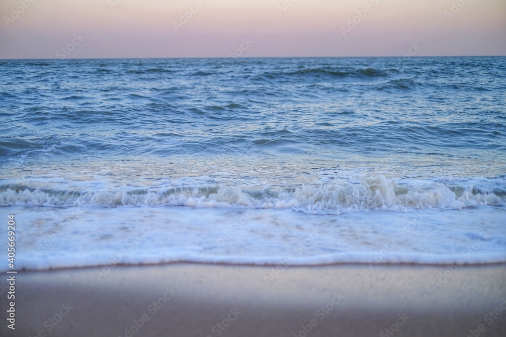 Obraz premium A shot of a vase sea view from the edge of a beach just before sunset with golden light in the sky and foamy sea water as it washup on the sandy beach.
