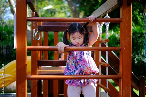 A cute young Asian girl is playing at a playground, trying to climb a ladder having fun and feeling happy. © Sirichai