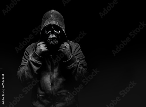 Horror photo of a scary man in hoodie with skull face on black background.