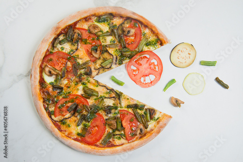 Italian veggie Pizza on white marble background with ingredients: tomato, eggplant, zucchini slices, champignon mushrooms and green beans. Flying food concept. Vegetarian pizza served with pesto sauce