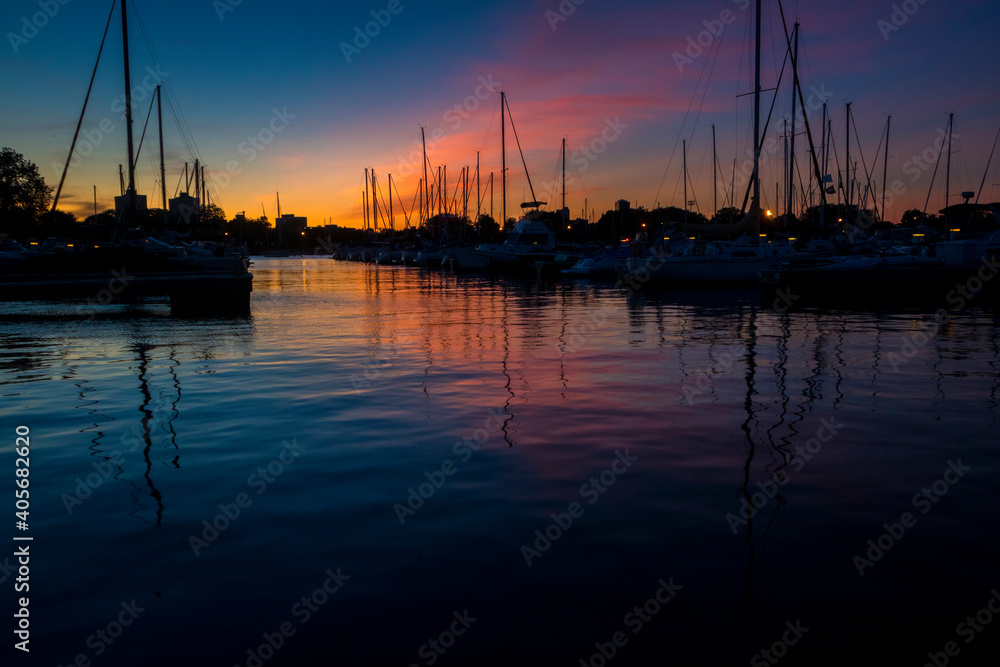 Boats sit on water in a harbor during a colorful sunset.