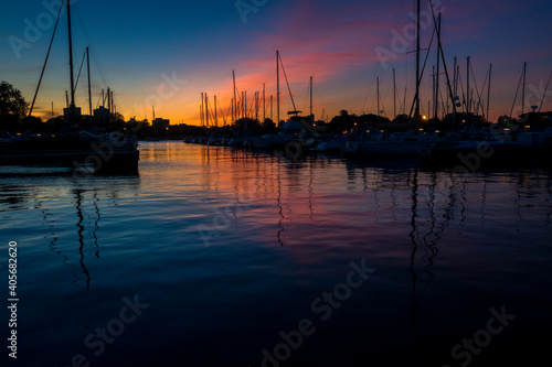 Boats sit on water in a harbor during a colorful sunset.