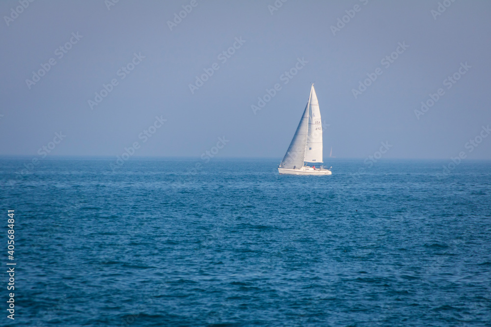 White sail boat on the horizon of blue waters.