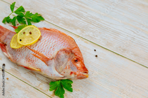 Raw red tilapia fish with herbs and lemon on wooden background. Top view.