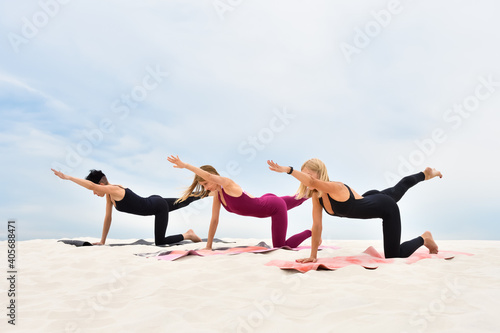 Three beautiful young women perform yoga exercises on the beach