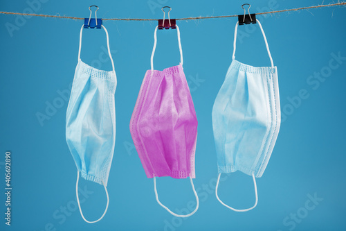 Three medical masks hanging on a rope, pink and blue on a blue background.