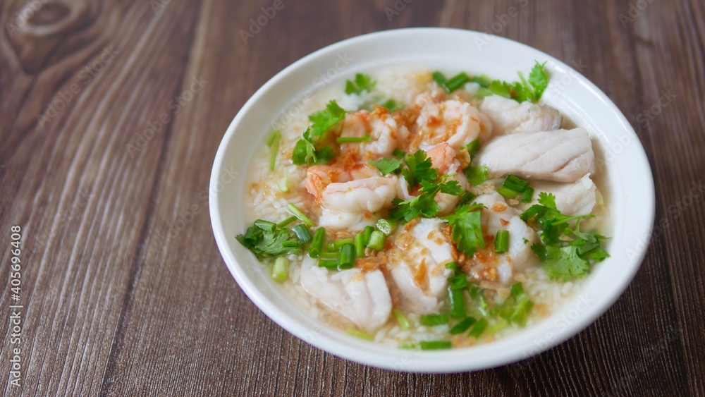 Boiled rice soup with fish and shrimp in bowl on wood background Boiled rice soup with fish and shrimp in bowl on wood background