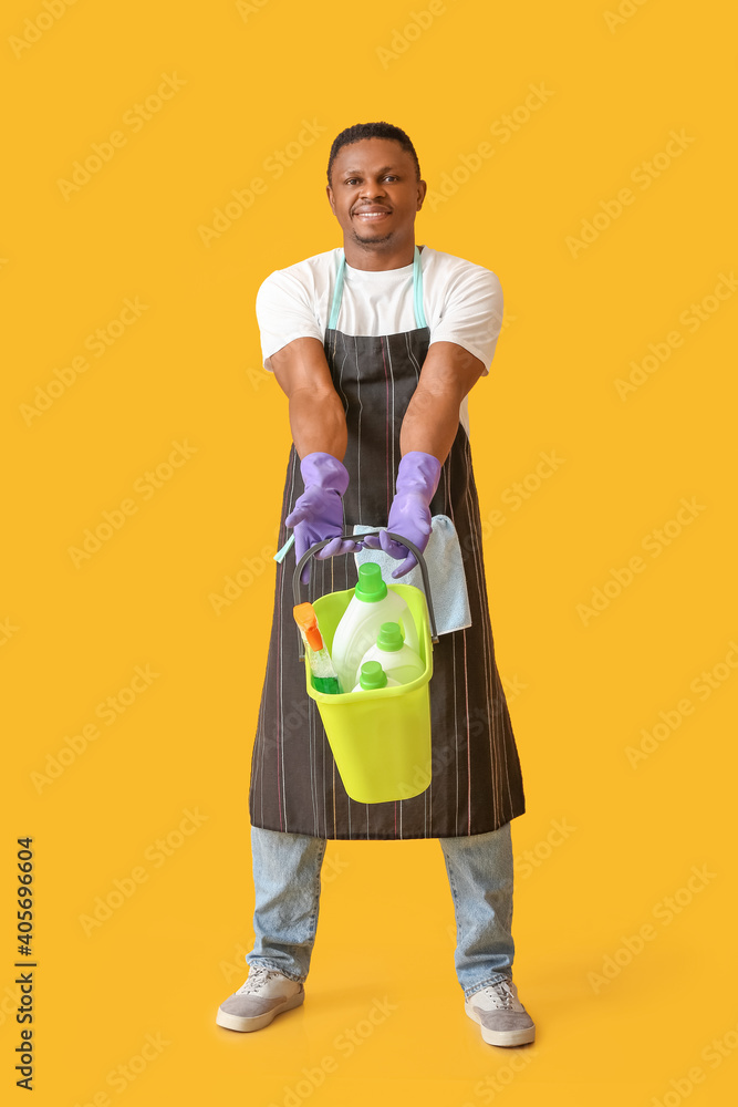 African-American man with cleaning supplies on color background African-American man with cleaning supplies on color background