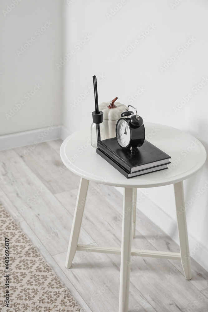 Table with books, alarm clock and decor near white wall