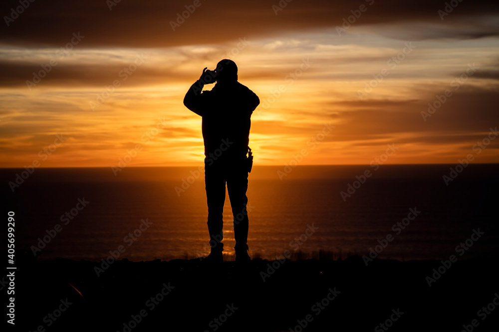 Silhouette of a man looking out at a sunset or sunrise taking a cell phone picture