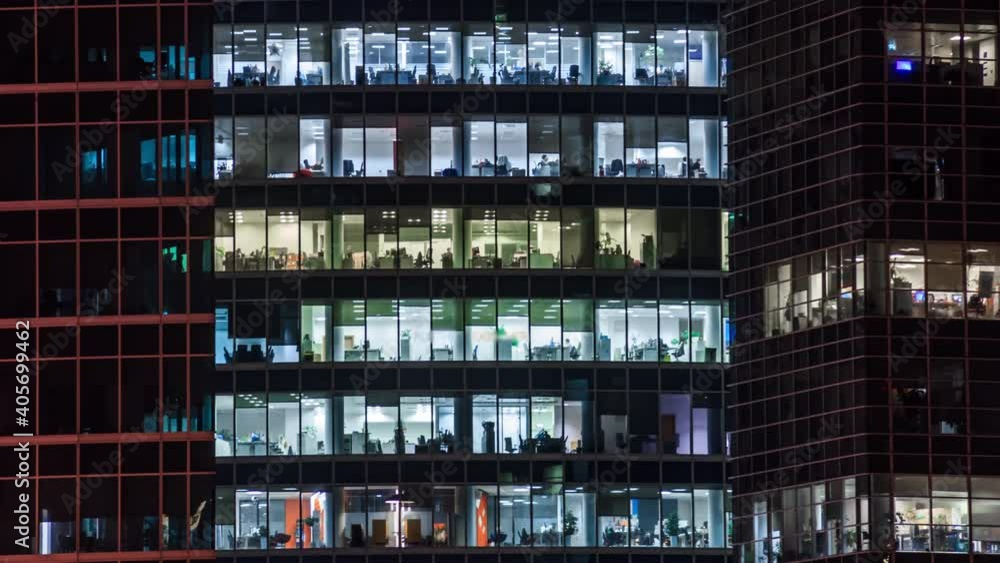 Modern office building with large windows at night, light shines in the windows Modern office building with large windows at night, light shines in the windows