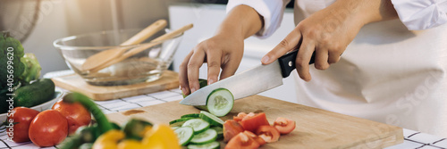 Bild auf Leinwand Woman using knife and hands cutting cucumber on wooden board in kitchen room