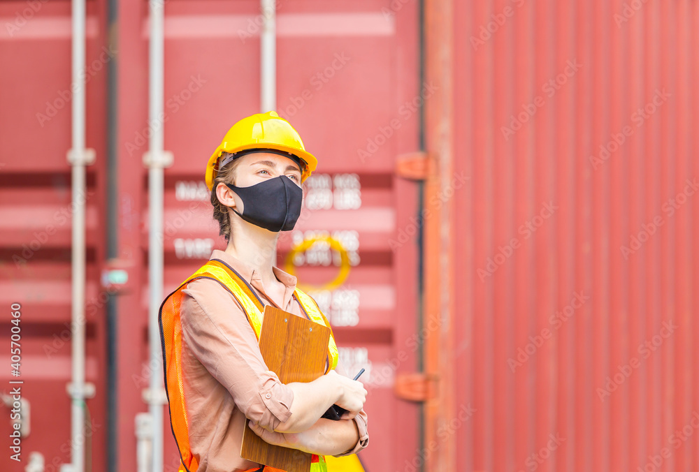 Engineer in hardhat and safety vest holding clipboard checklist and two-way radio, Woman wearing protection face mask against coronavirus at containers cargo Engineer in hardhat and safety vest holding clipboard checklist and two-way radio, Woman wearing protection face mask against coronavirus at containers cargo
