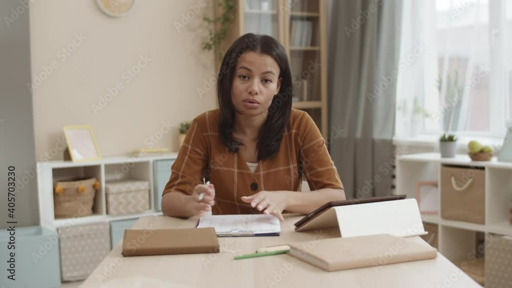 Medium close-up POV of Mixed-Race young woman sitting by desk in room, talking angrily and looking on camera, showing clipboard with paper Medium close-up POV of Mixed-Race young woman sitting by desk in room, talking angrily and looking on camera, showing clipboard with paper