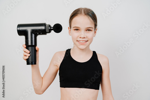 teen girl holds massage gun. medical-sports device helps to reduce muscle pain after training, helps to relieve fatigue, affects problem areas of body, improves condition of skin. © Maria