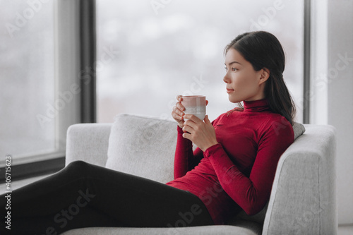 Happy Asian woman relaxing at home during coronavirus lockdown feeling calm and positive enjoying drinking coffee alone indoors. Mental health, wellness, well-being.