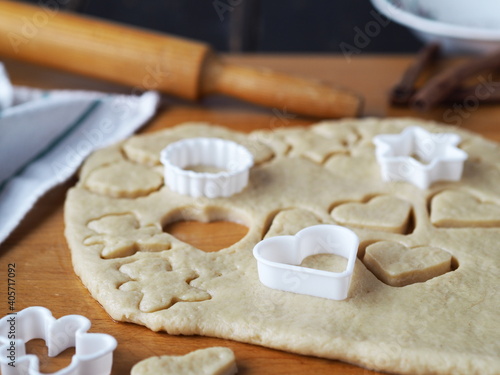Raw shortbread cookies cut from a layer of dough with cookie cutters on a kitchen board on a dark wooden table.Confectionery background.