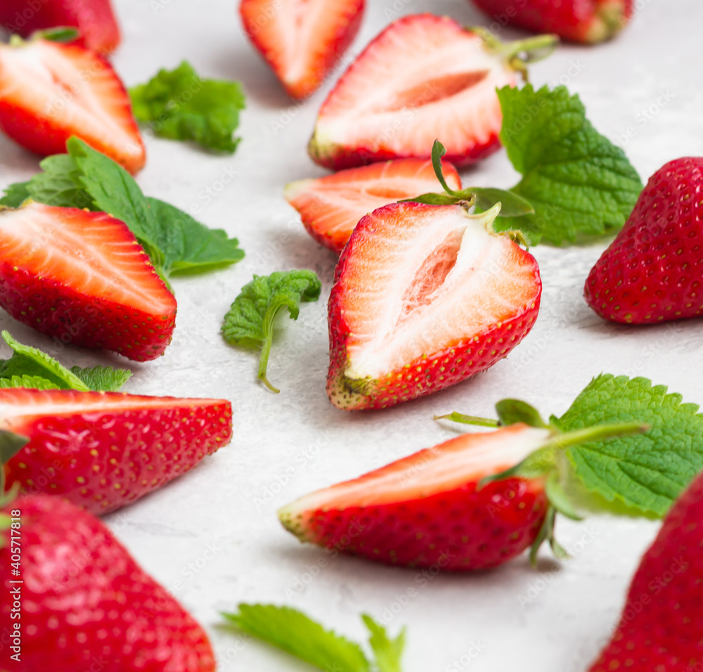 Composition with whole and sliced strawberries and mint leaves on a grey background. Close up. Composition with whole and sliced strawberries and mint leaves on a grey background. Close up.
