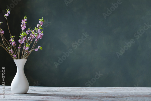 daphne flowers in vase on old wooden table on background green wall photo